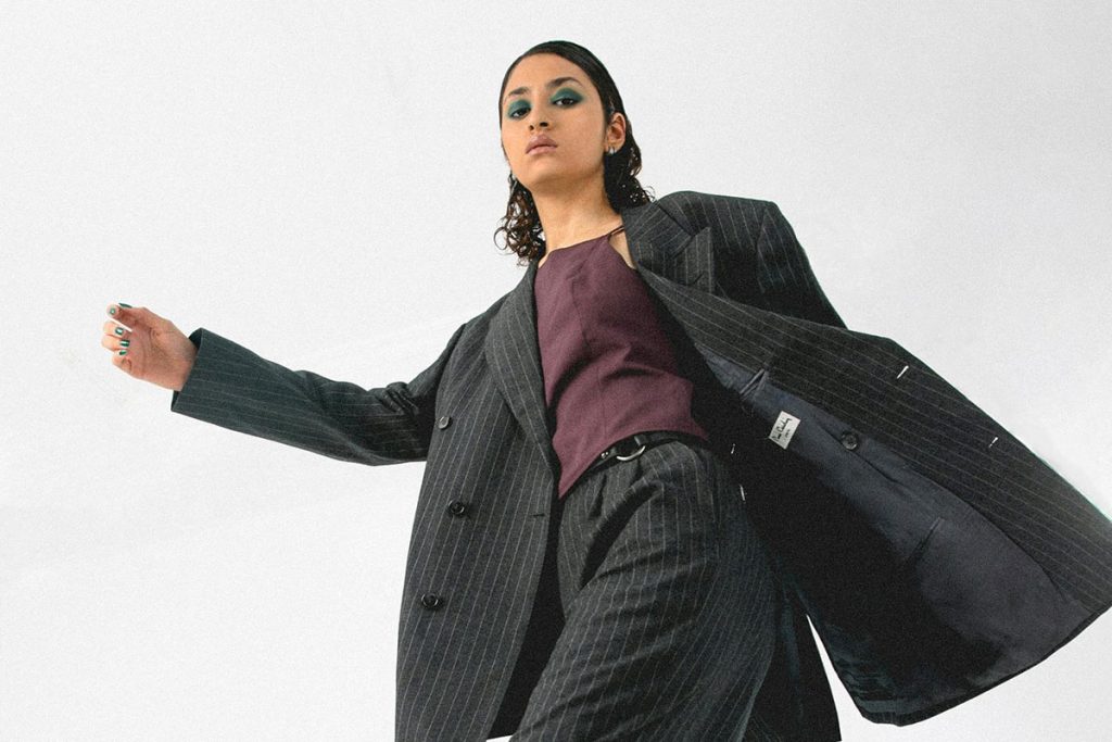 Person in a pinstripe suit and purple shirt poses confidently against a white background.