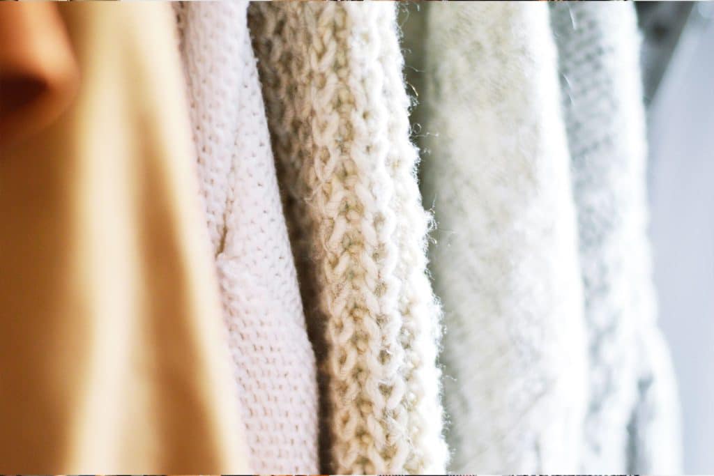 Close-up of assorted knit and woven fabrics in soft, neutral colors hanging side by side.