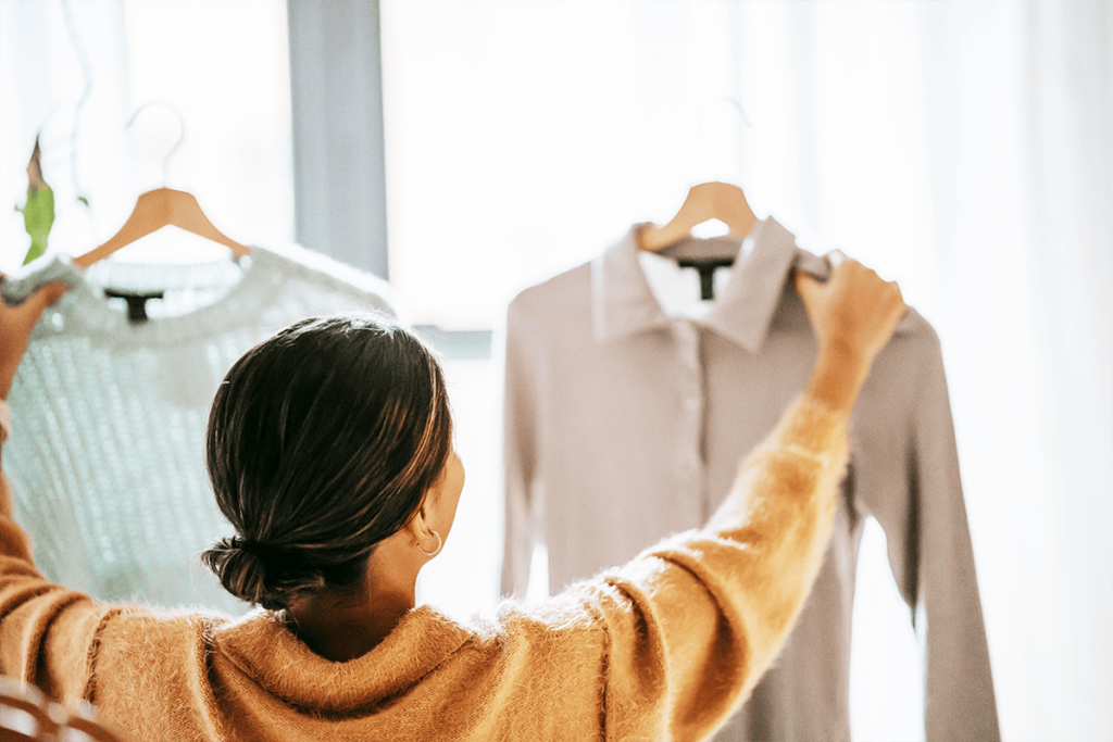 A person holds up two sweaters on hangers, deciding which one to wear.