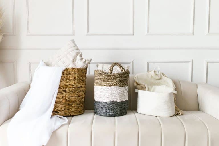 Three woven baskets with pillows and blankets on a cream-colored sofa against a white wall.
