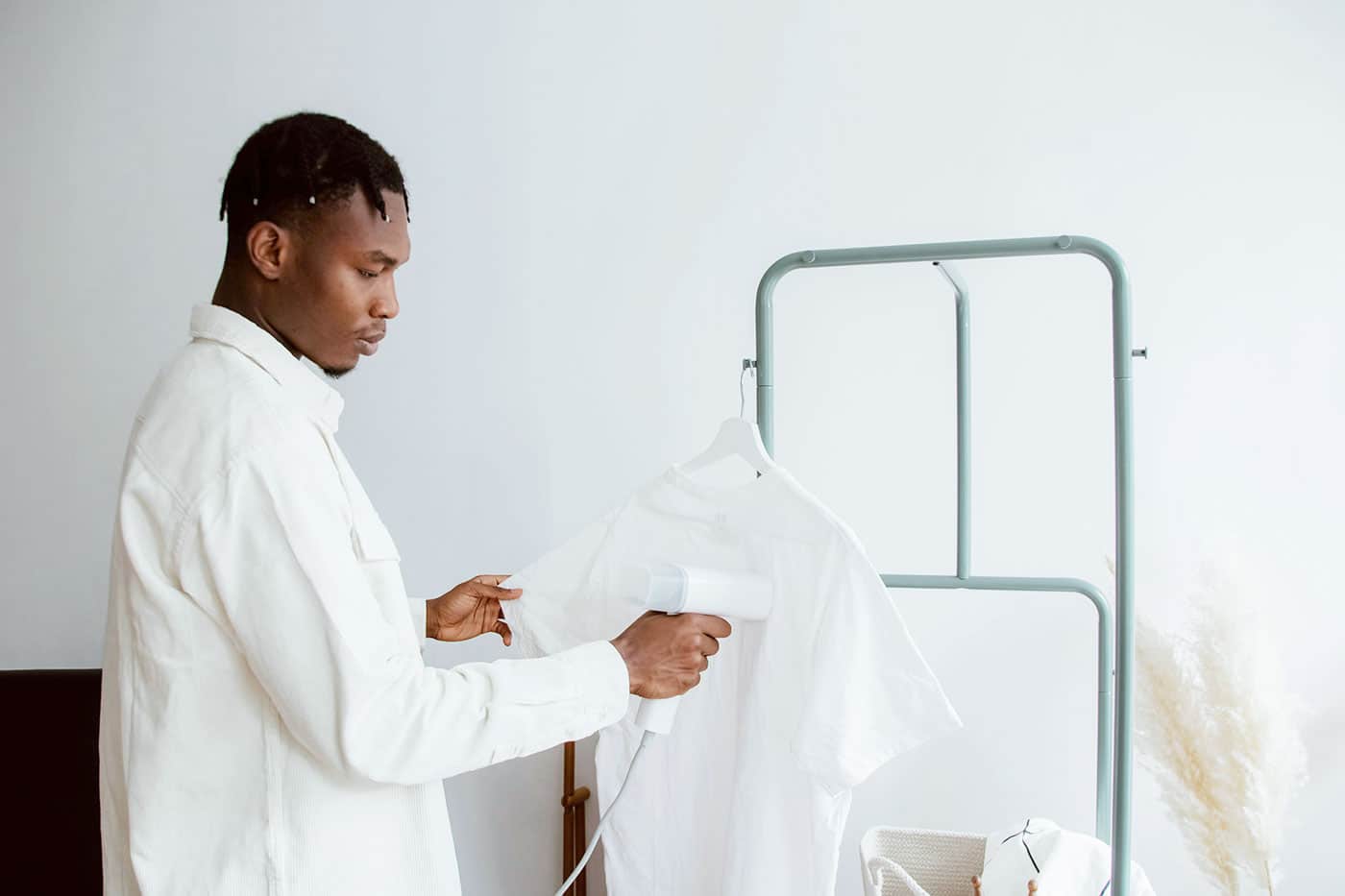 Person steaming a white shirt on a hanger with a handheld garment steamer.