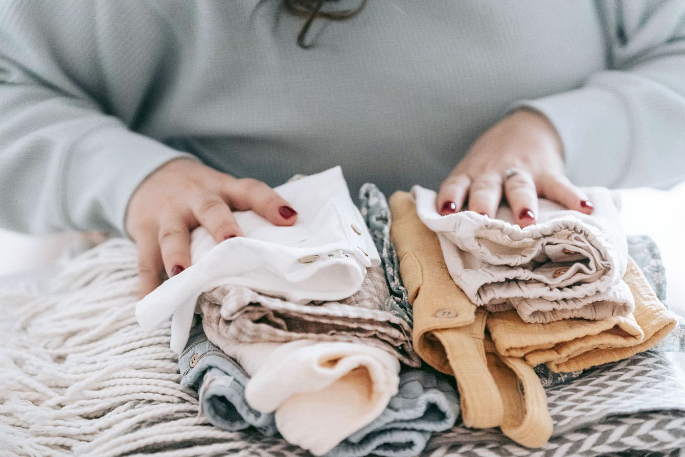 Person with red nails organizing folded baby clothes on a soft surface.