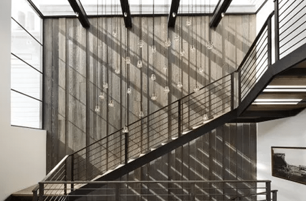 Modern staircase with hanging lights and sunlight casting shadows on a wooden wall.