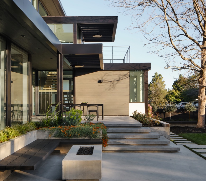 Modern home exterior with concrete steps, patio seating, and landscaped garden beds.