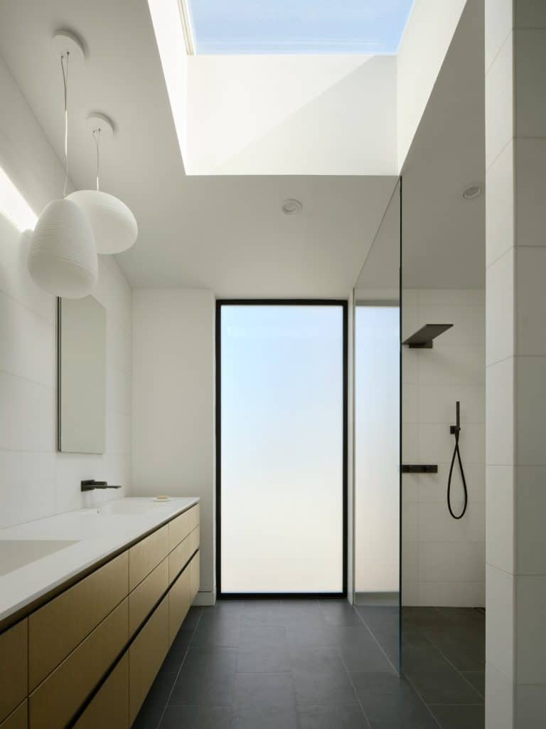 Minimalist bathroom with skylight, frosted glass door, wood cabinets, and walk-in shower.