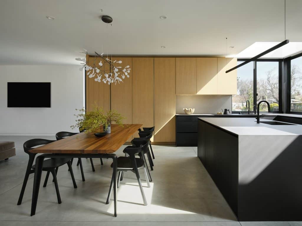 Modern kitchen and dining area with wood cabinetry, black island, and large windows.