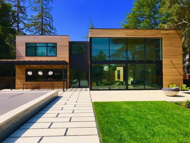 Modern two-story house with large glass windows, wood siding, and a landscaped yard.