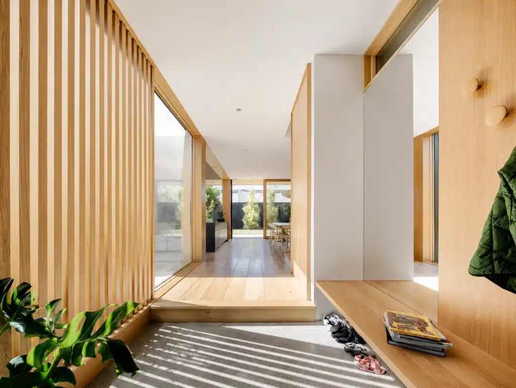 Bright, modern hallway with wood paneling, bench, coat hook, shoes, and magazine.