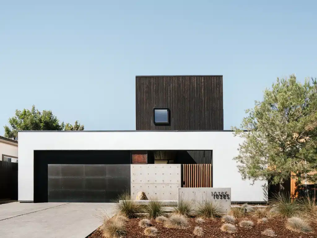 Modern two-story house with black and white facade, flat roof, and minimalist landscaping.