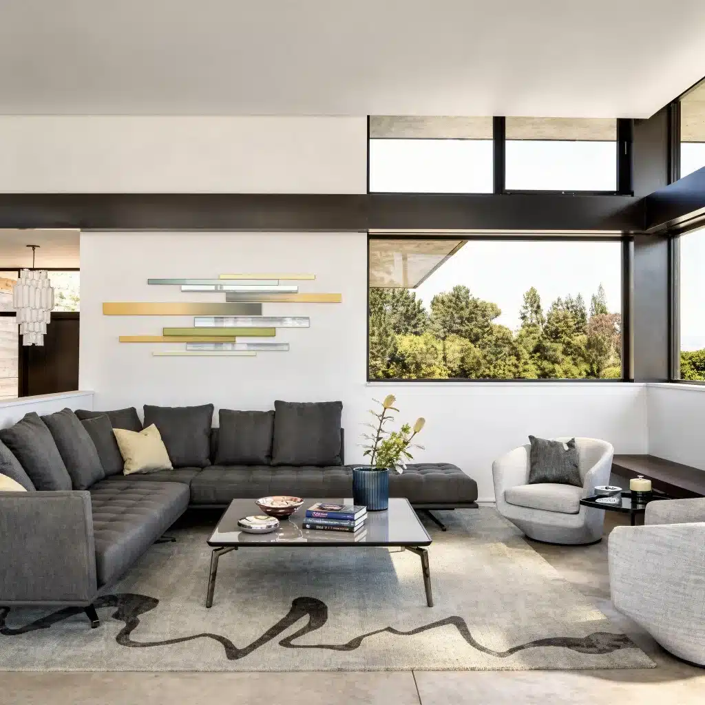 Modern living room with gray sectional sofa, abstract wall art, and large windows with a view.