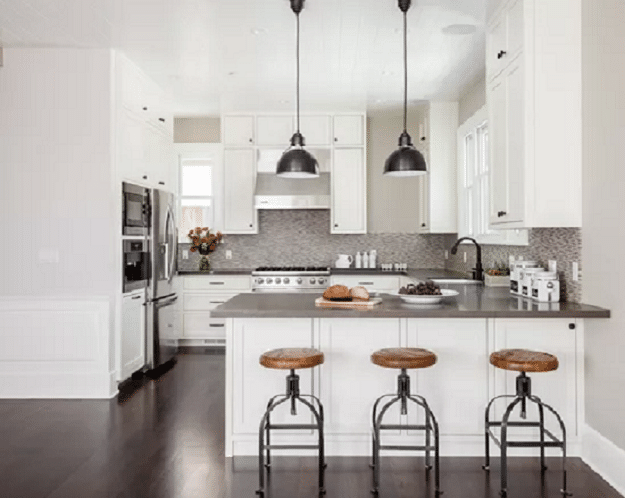 Modern white kitchen with island, bar stools, pendant lights, and stainless steel appliances.